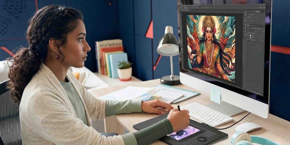 Young Indian woman drawing digital art on a graphics tablet with Photoshop open on monitor